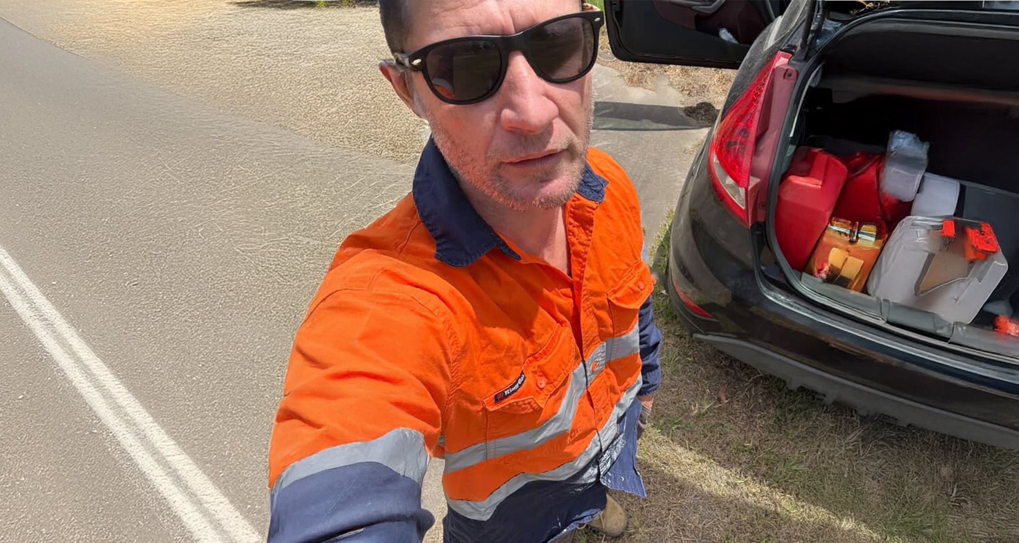 Man in high-visibility clothing standing next to an open car trunk with supplies.